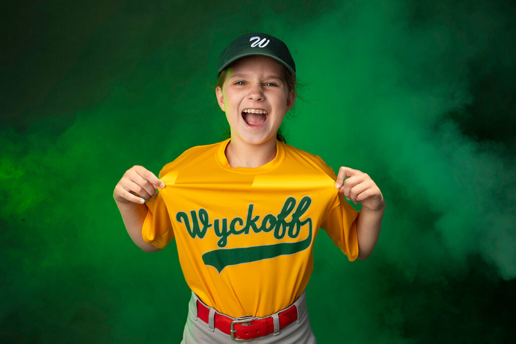 A young boy holding up his baseball uniform.