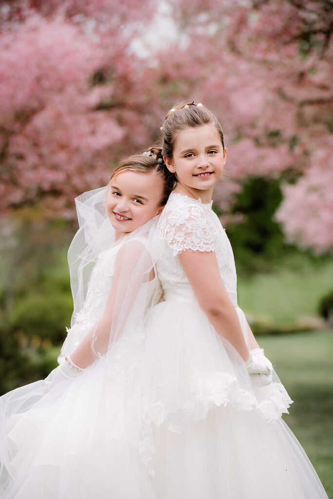 First Communion portrait of two girls in a trail of pink cherry blossom trees in New Jersey with natural light.