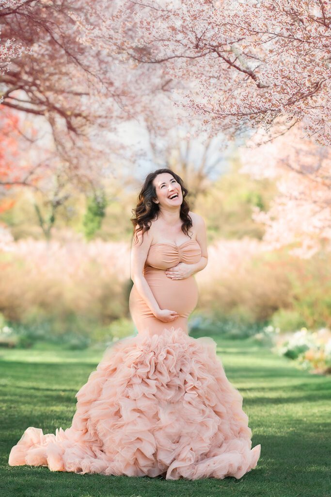 Maternity photography session in Northern NJ garden with pink cherry blossom trees wearing a peach gown